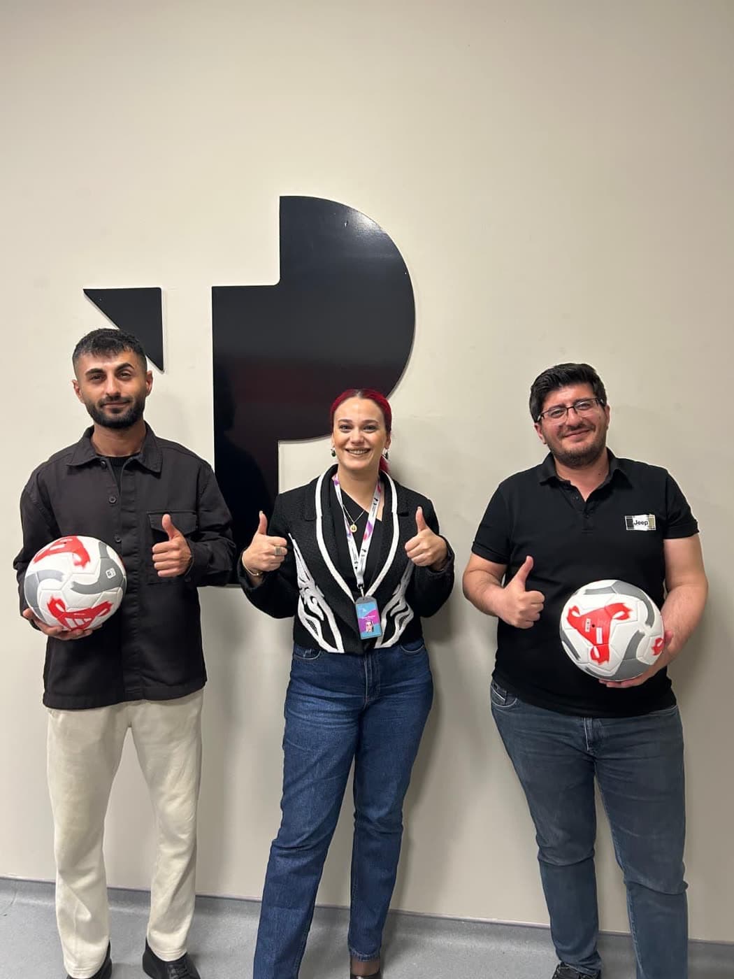 Üç çalışan TP logosunun önünde futbol toplarıyla poz veriyor